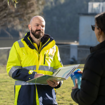 Person in Hydro Tas high-vis and holding a clipboard speaking to a stakeholder in the foreground