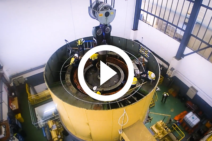 The disassembly of a turbine at Lake Echo power station. A large blue cylinder with parts being assembled within by 6 workers in high-vis. Wires hang overhead to lift the disassembled pieces out of the machine.