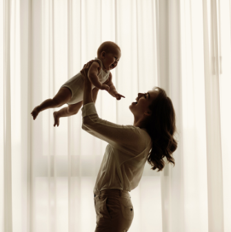 A mum holding their young infant up in the air and smiling