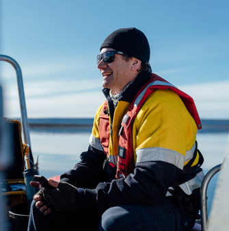 Person wearing high-vis and lifejacket on a boat, smiling