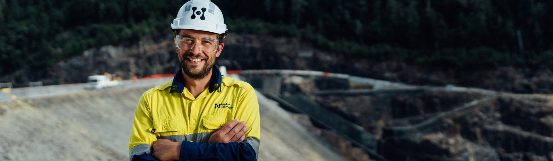 Person wearing high-vis and Hydro Tas hardhat smiling for camera in front of worksite