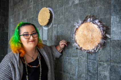 Bianca Templar smiling for a portrait with her artwork From Coast to Country, displayed on the wall.